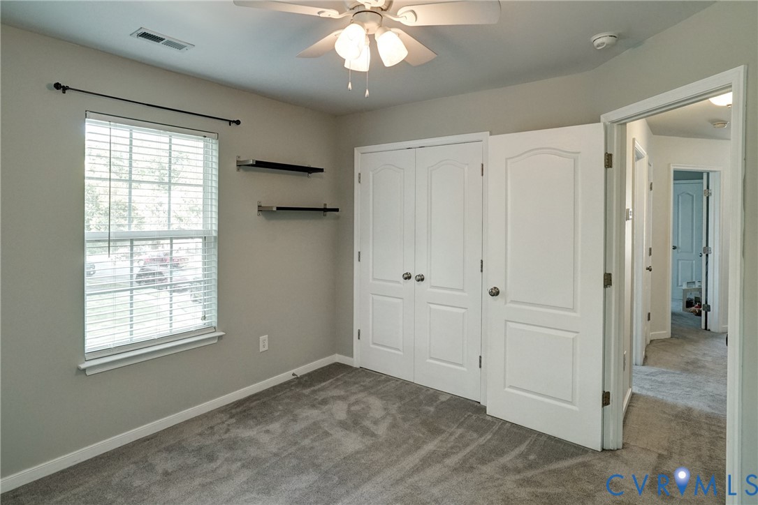 Interior space featuring neutral wall tones, wall-to-wall carpeting, a double-door closet, multi-tier wall shelving, and a ceiling-mounted light fixture