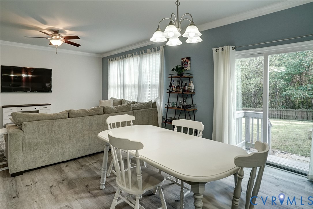 Living area featuring wood-finish flooring, crown molding, a ceiling fan, a five-light chandelier, and a sliding glass door