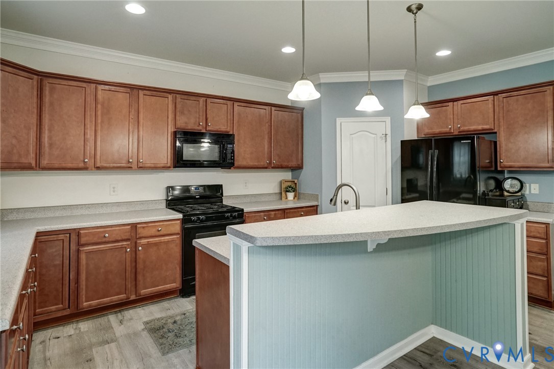 Kitchen featuring wood cabinetry, stone-finish countertops, an island with beadboard paneling, recessed lighting, and a trio of pendant lights