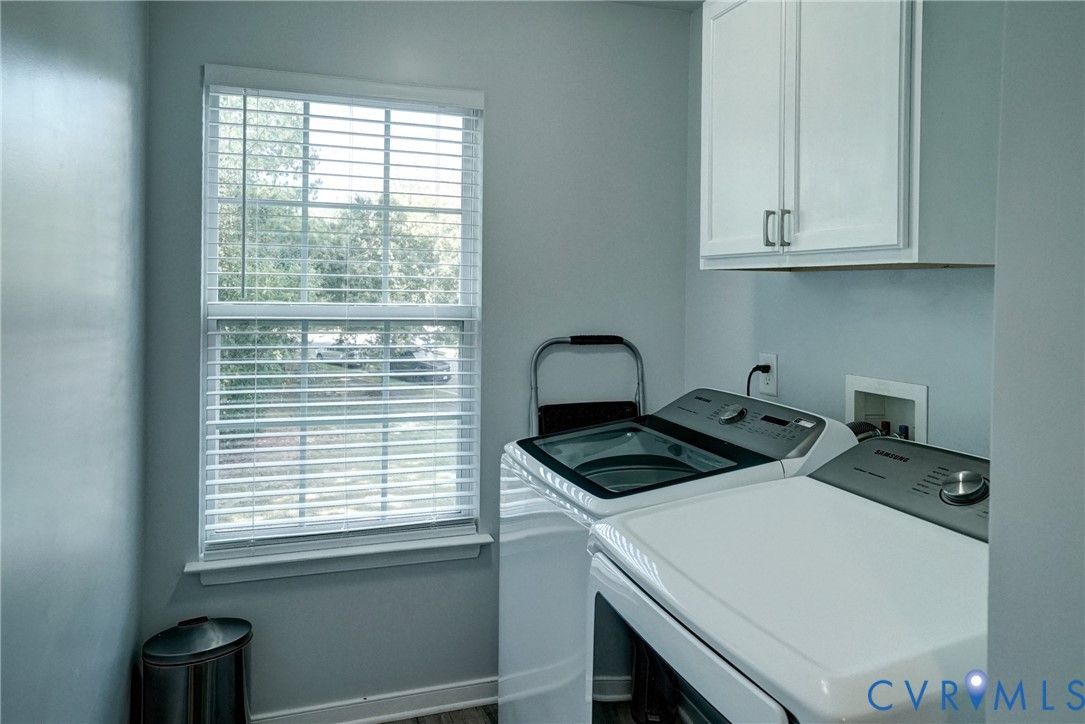 Laundry room featuring white wall-mounted upper cabinetry, a double-hung window with blinds, and dedicated hookups for laundry appliances