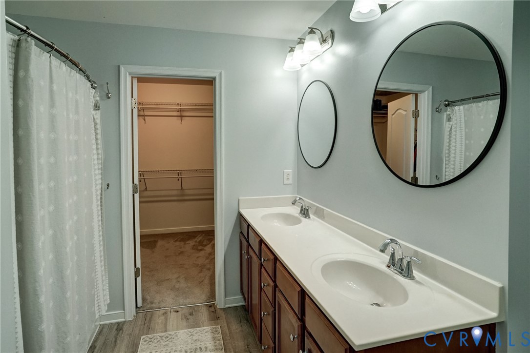 Double vanity with a solid-surface countertop, dual undermount sinks, round wall mirrors, and wood-finish cabinetry