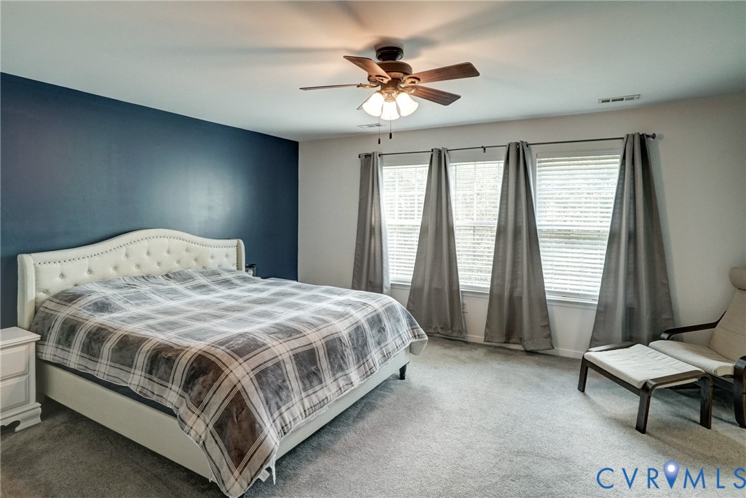 Room featuring a deep blue accent wall, neutral carpeting, and a multi-light ceiling fan