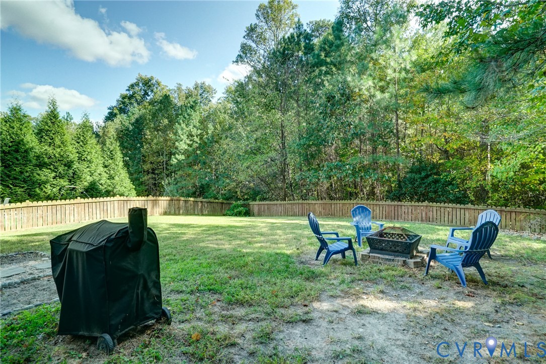 Expansive backyard featuring a wood-style perimeter fence, mature tree line, and stone-bordered fire pit area Expansive backyard featuring a wood-style perimeter fence, mature tree line, and stone-bordered fire pit area