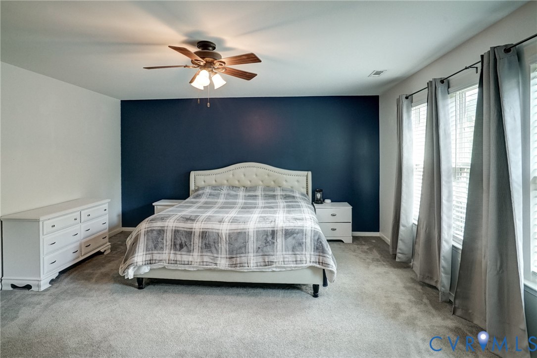 Room featuring wall-to-wall carpeting, a deep navy accent wall, and a multi-blade ceiling fan with integrated light fixture