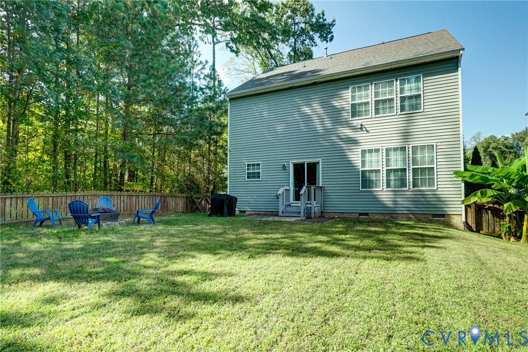 Two-story residence featuring light gray horizontal siding, an expansive rear lawn, perimeter wood fencing, a dedicated stone fire pit area, and a rear exterior staircase Two-story residence featuring light gray horizontal siding, an expansive rear lawn, perimeter wood fencing, a dedicated stone fire pit area, and a rear exterior staircase