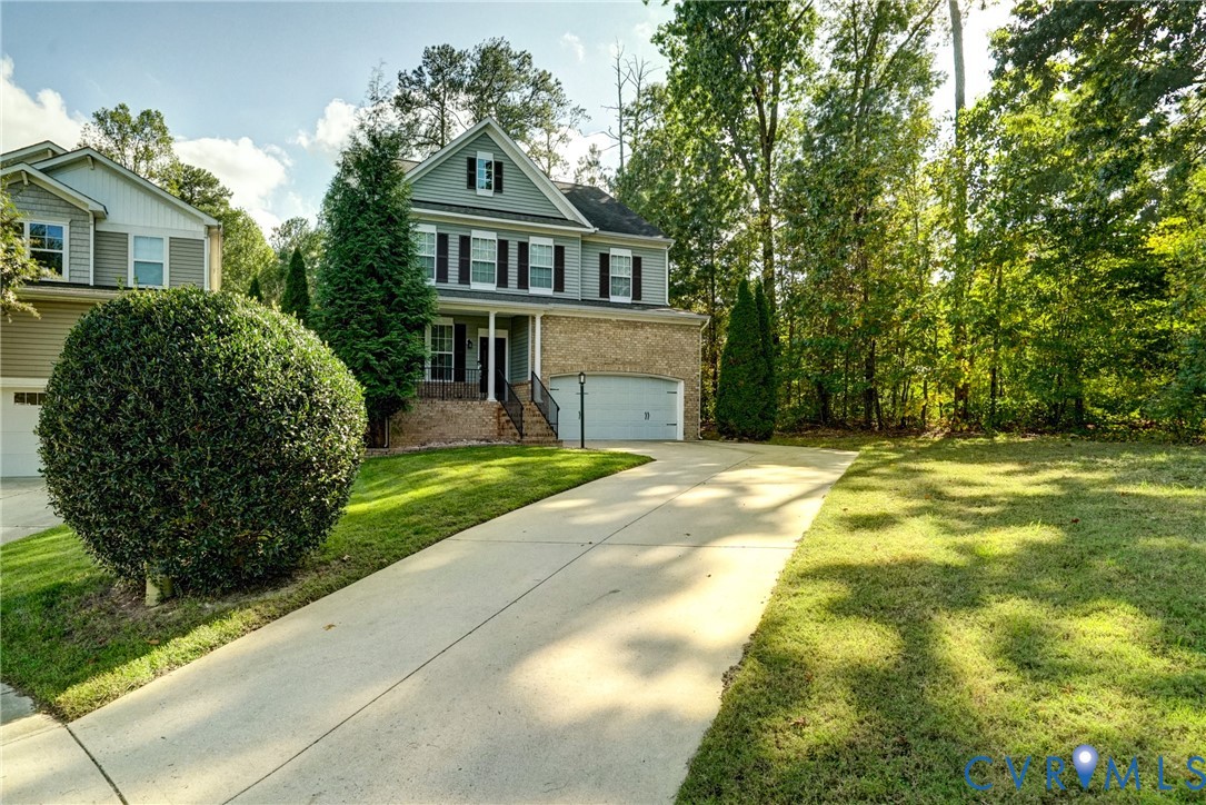 Two-story residence featuring a brick and horizontal siding exterior, a front-facing attached garage, a covered entryway with decorative railings, and a concrete driveway situated on a wooded lot Two-story residence featuring a brick and horizontal siding exterior, a front-facing attached garage, a covered entryway with decorative railings, and a concrete driveway situated on a wooded lot