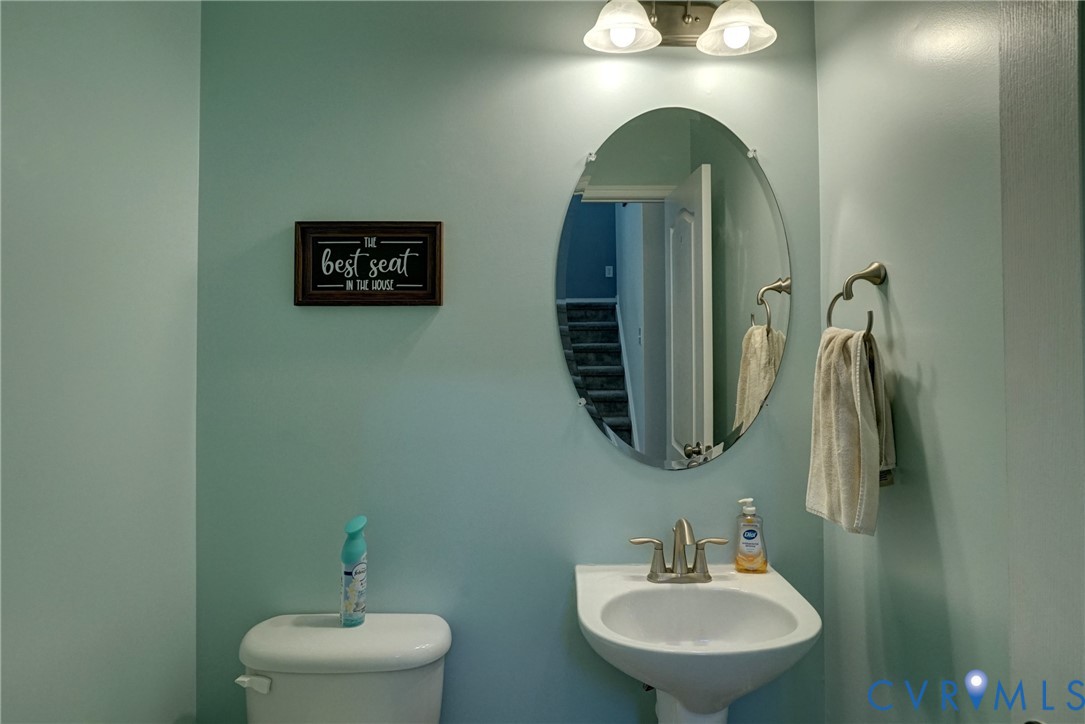 Wall-mounted oval mirror, pedestal sink with dual-handle faucet, and two-light vanity fixture