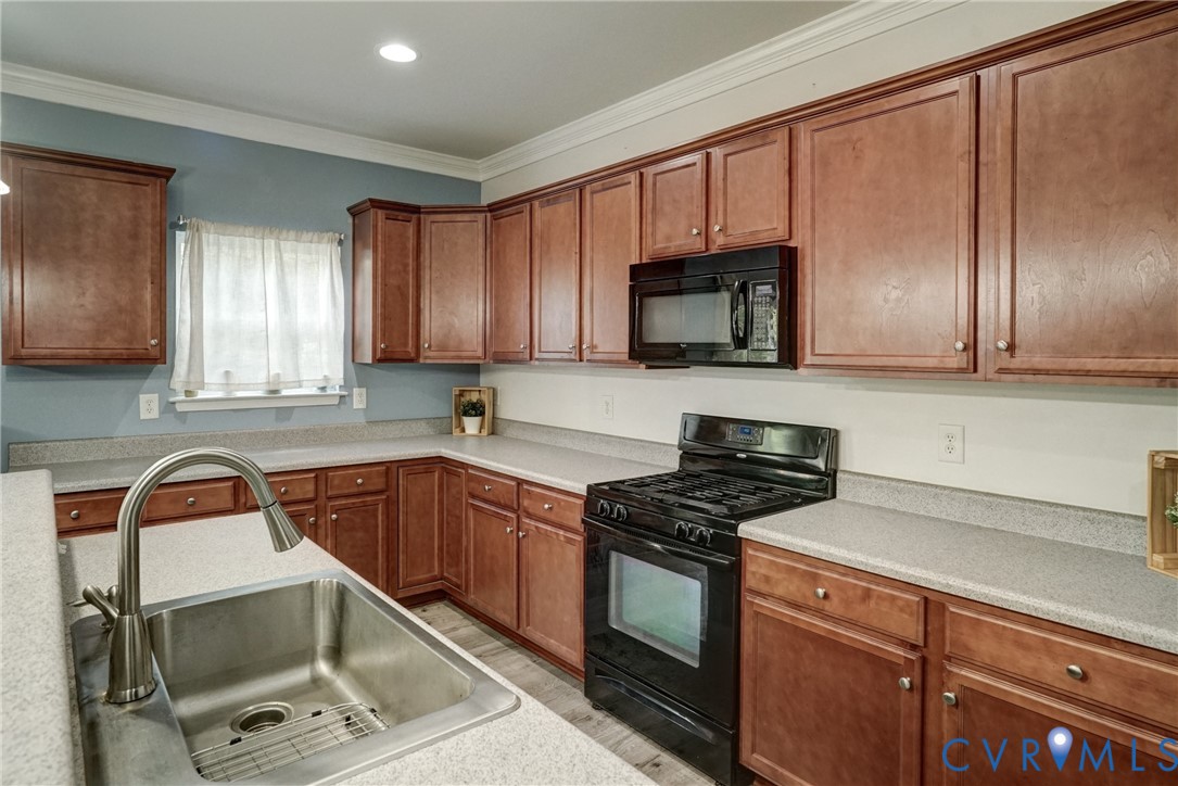 Kitchen featuring stained wood cabinetry, stone-finish countertops, stainless steel undermount sink with a high-arch pull-down faucet, and a black built-in microwave and range
