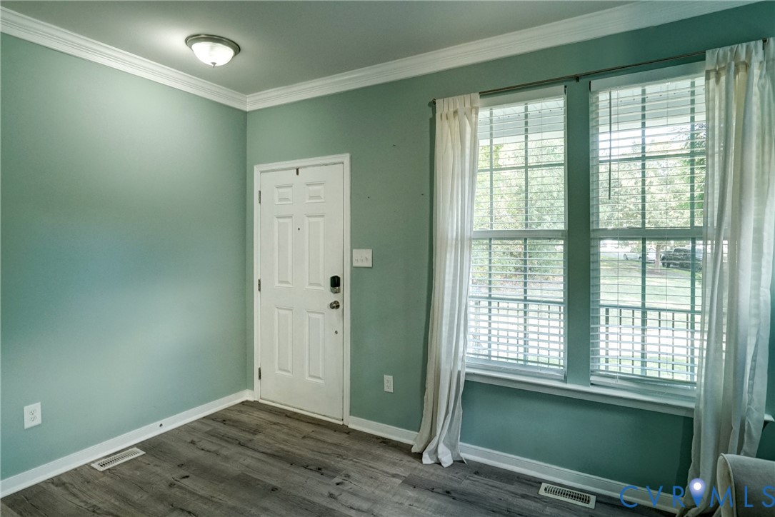 Room featuring wood-finish flooring, crown molding, double-pane windows with muntins, and a six-panel exterior door