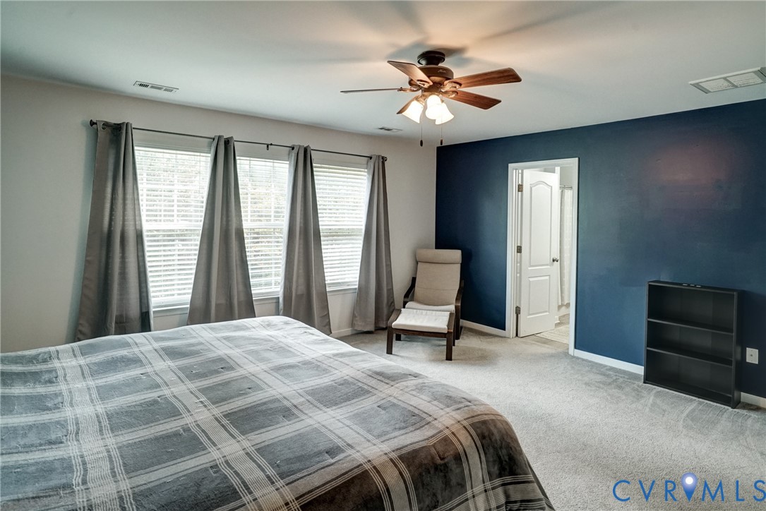 Room featuring neutral carpeting, a dark accent wall, a central ceiling fan with integrated lighting, and multiple windows with blinds