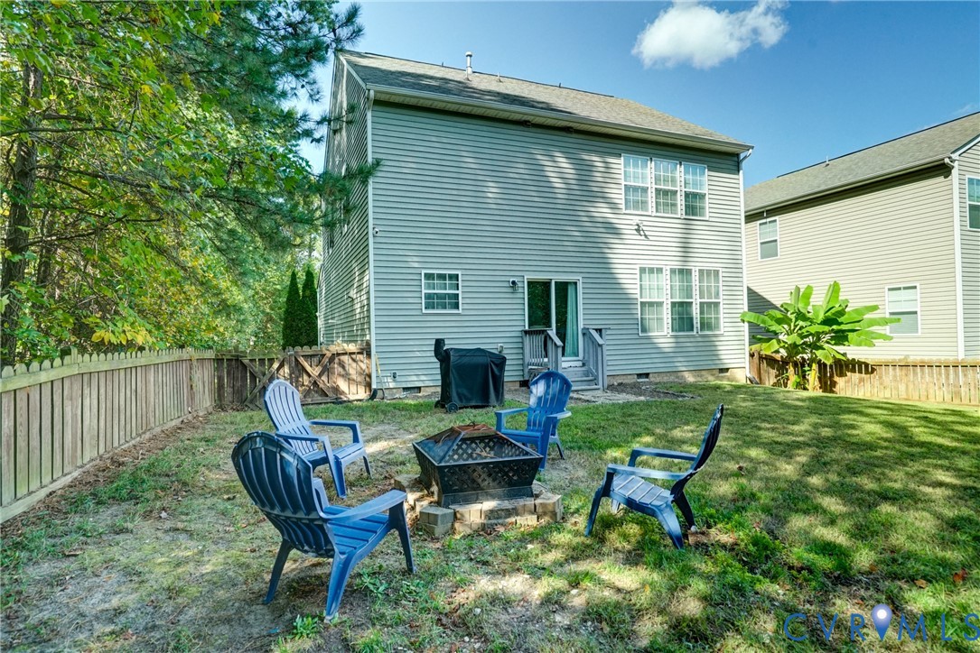 Rear exterior featuring light-toned horizontal siding, a fenced backyard, and mature trees