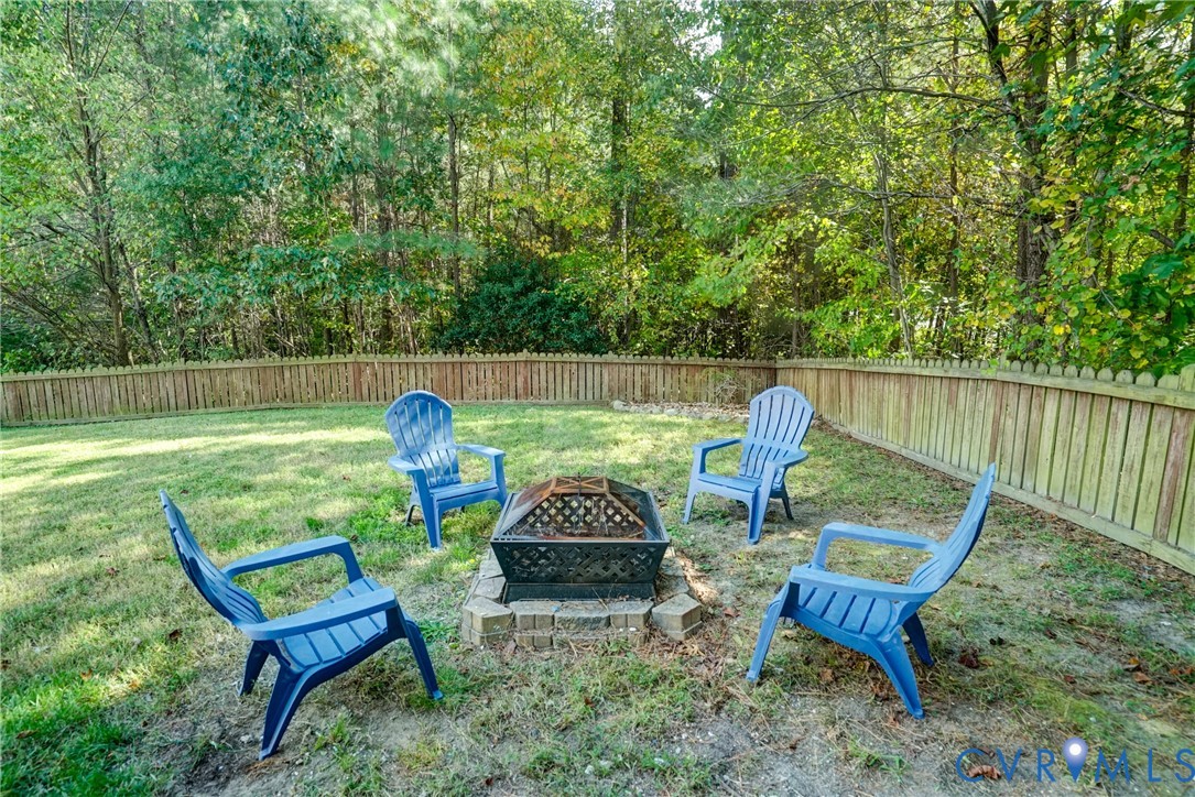 Backyard featuring a stone-lined fire pit, enclosed by a wood privacy fence and bordered by mature trees Backyard featuring a stone-lined fire pit, enclosed by a wood privacy fence and bordered by mature trees
