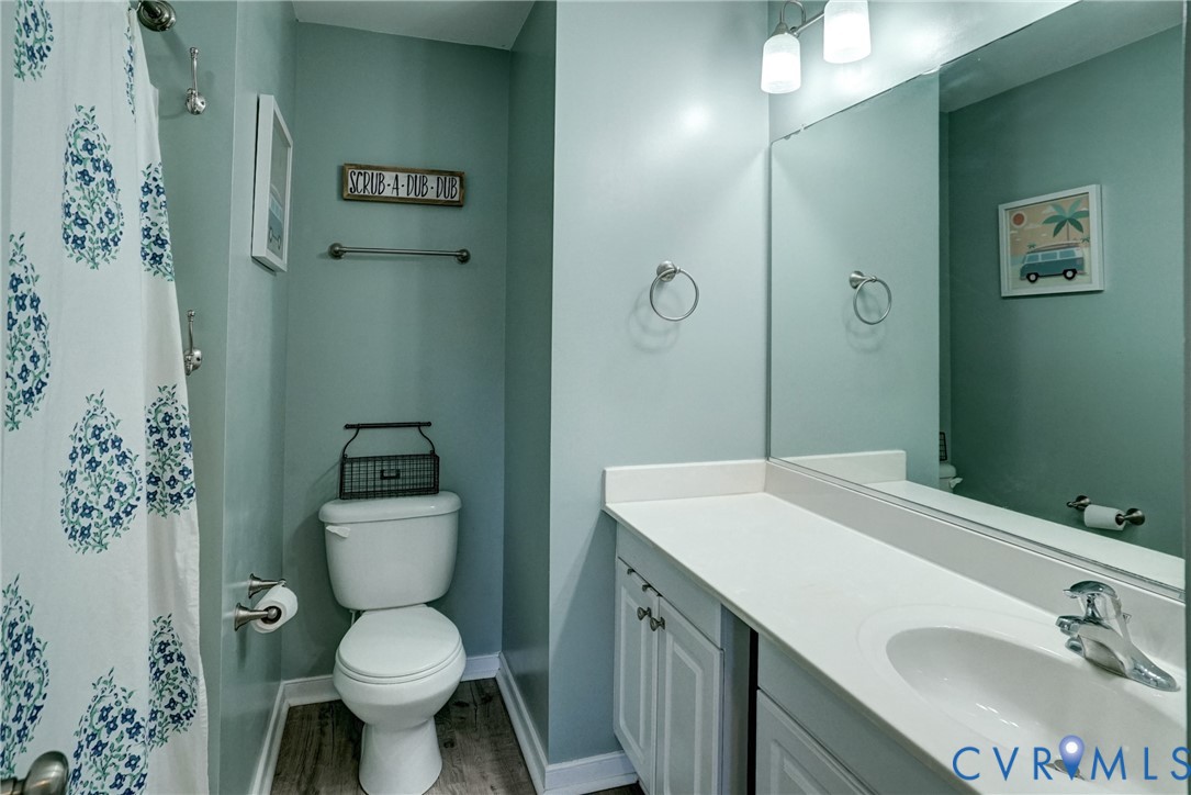 Bathroom featuring a vanity with a white countertop and integrated sink, a full-width wall mirror, wood-finish flooring, and a combined tub and shower area