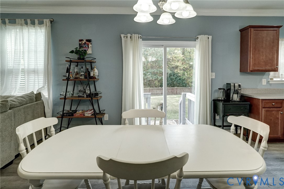 Dining area featuring glass sliding doors, wood-finish cabinetry, crown molding, and a five-light chandelier