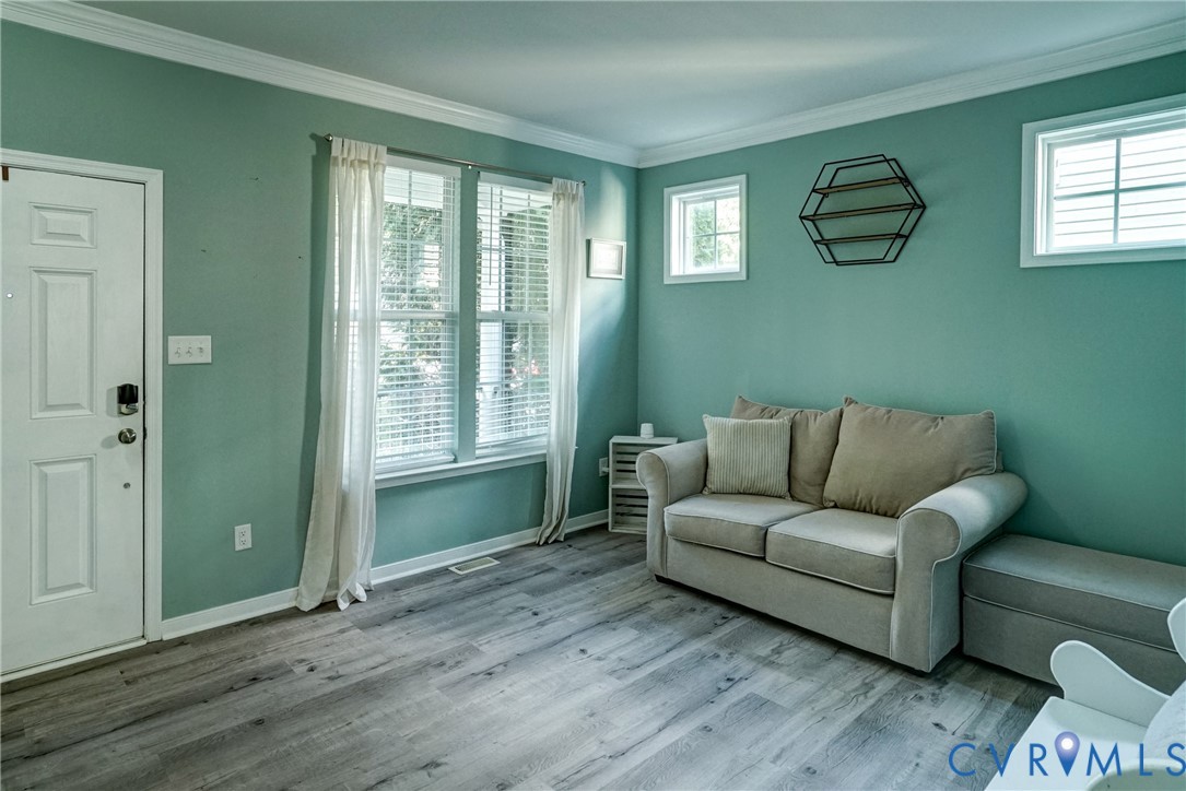 Interior space featuring wood-finish flooring, crown molding, double-hung windows with integrated shutters, and a six-panel exterior entry door