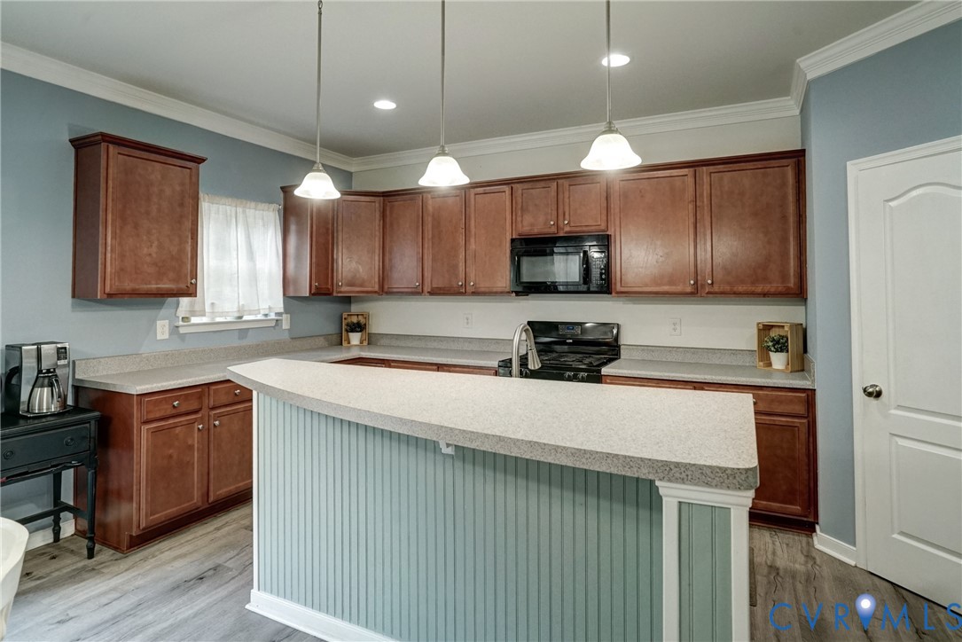 Kitchen featuring wood cabinetry, solid-surface countertops, beadboard-paneled breakfast bar, recessed lighting, and three hanging pendant lights