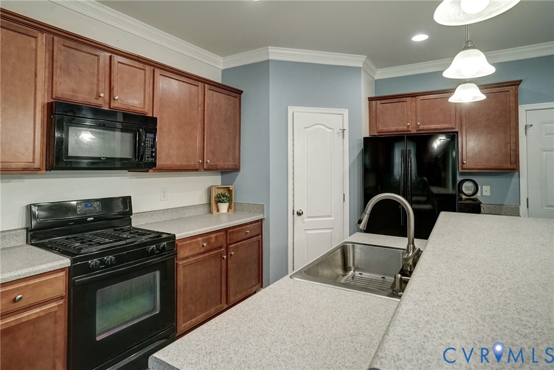 Kitchen featuring wood cabinetry, solid-surface countertops, black integrated appliances, stainless steel undermount sink with arched faucet, and crown molding