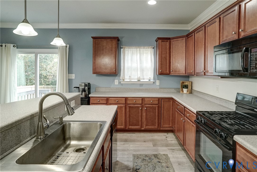 Kitchen featuring shaker-style wood cabinetry, stone-composite countertops, stainless steel undermount sink with arched pull-down faucet, black gas range with microwave, and wood-finish flooring