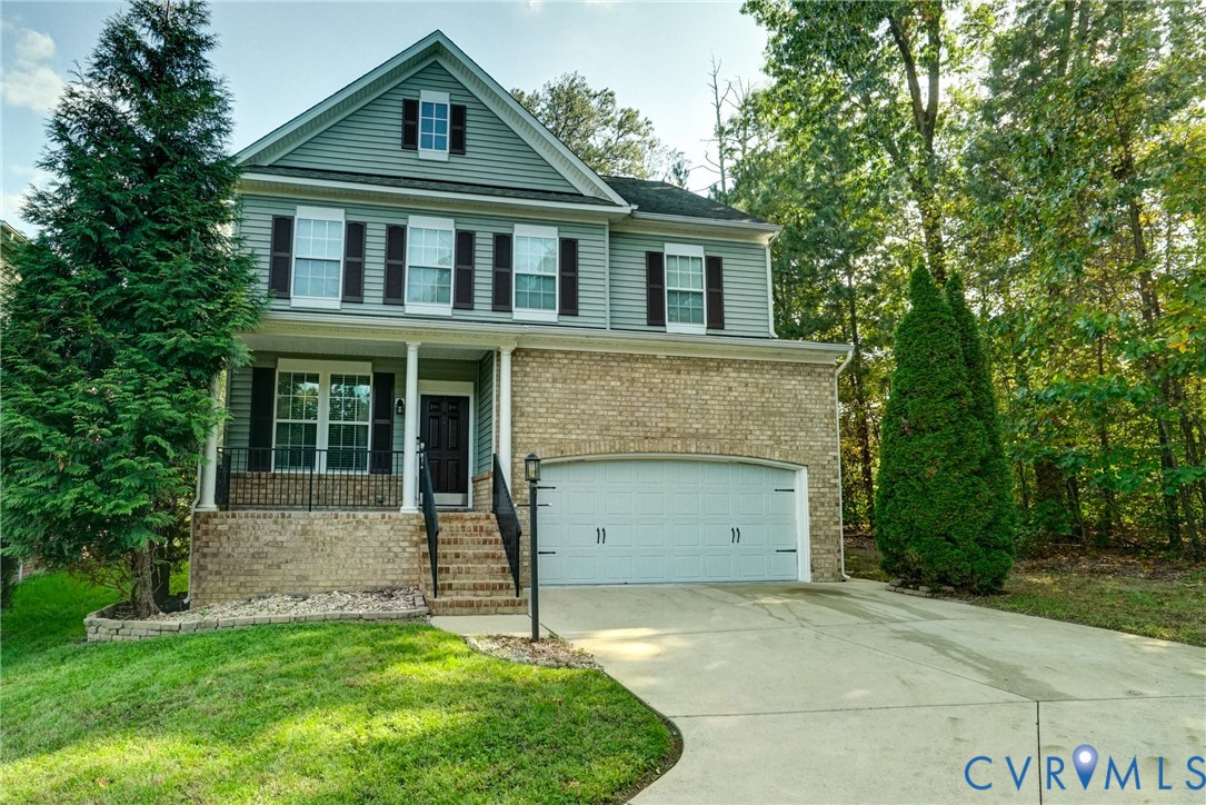 Two-story residence featuring a brick and horizontal siding exterior, attached two-car garage, front porch with metal railing, and decorative window shutters Two-story residence featuring a brick and horizontal siding exterior, attached two-car garage, front porch with metal railing, and decorative window shutters