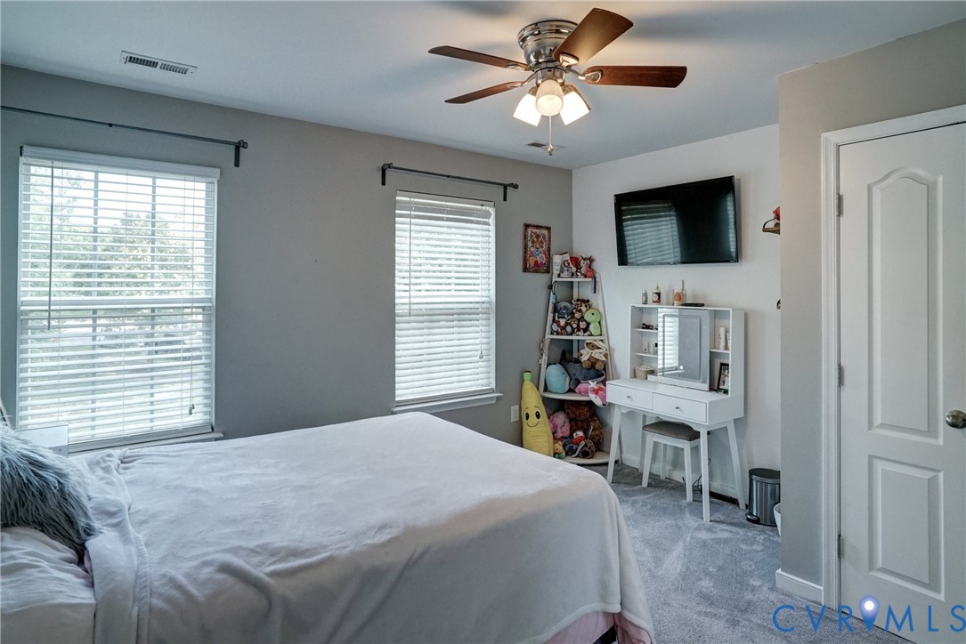 Neutral-toned interior featuring carpeted flooring, two windows with horizontal blinds, a ceiling fan with integrated lighting, and a six-panel door