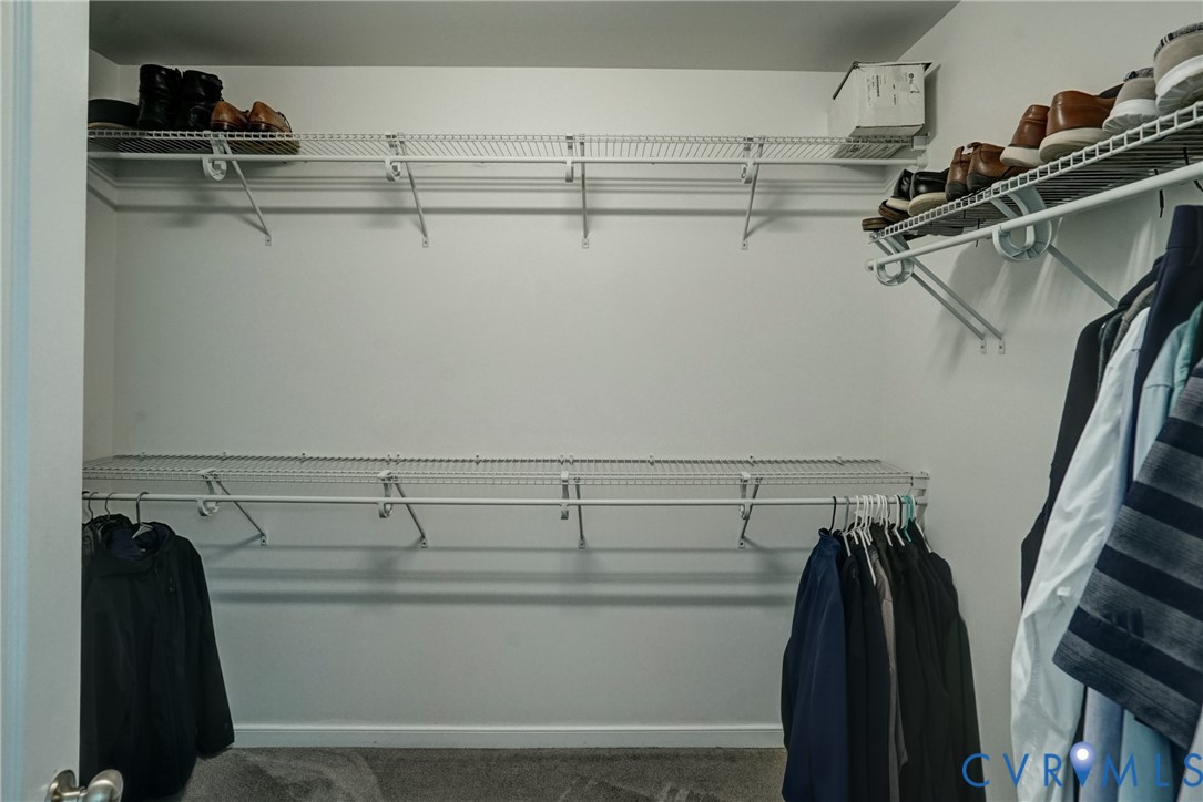 Walk-in closet featuring multi-tiered white wire shelving and integrated garment rods