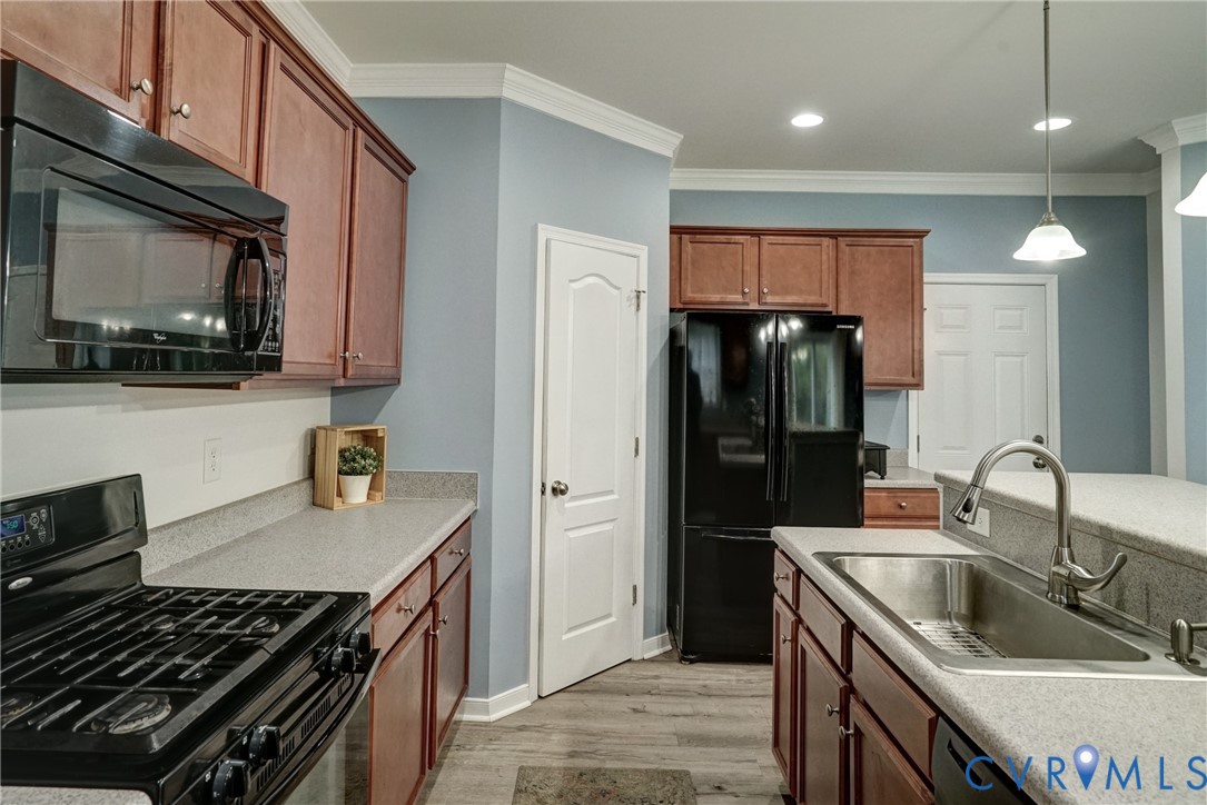Kitchen featuring stained cabinetry, stone-composite countertops, stainless steel sink with pull-down faucet, black appliance suite, and wood-finish flooring