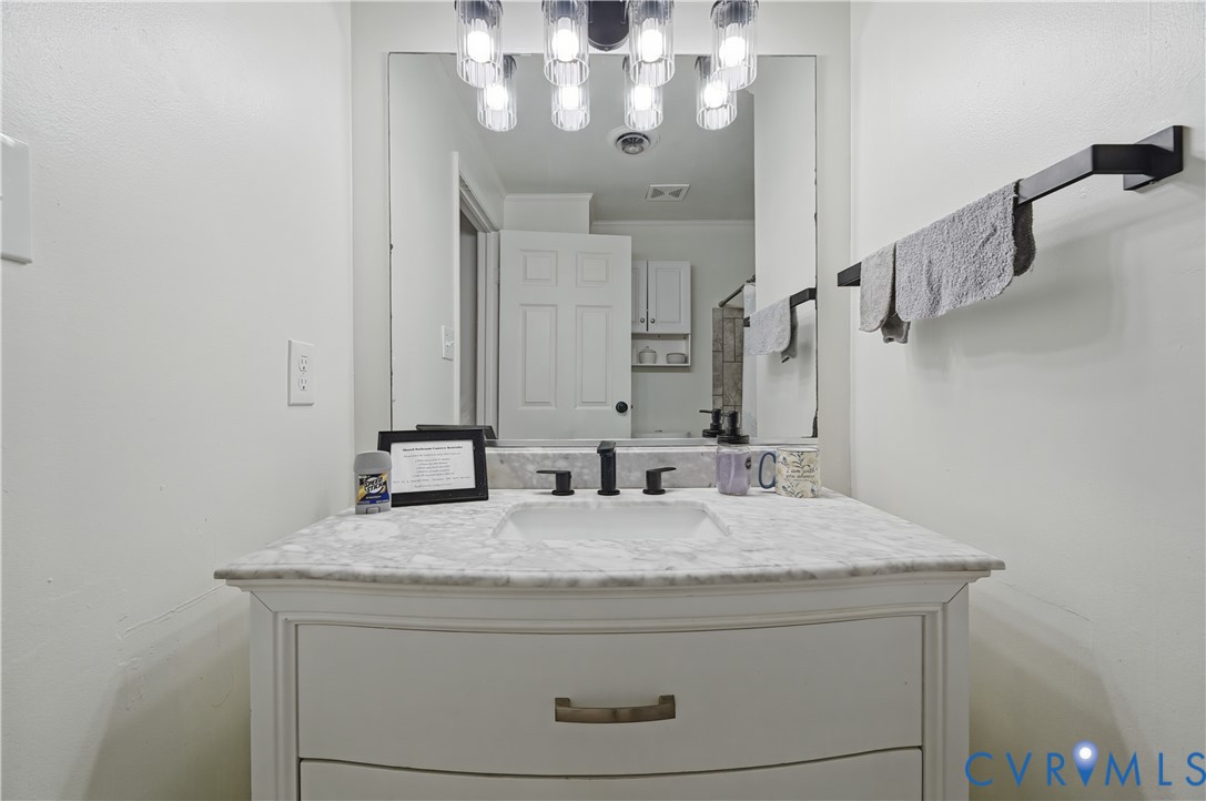 Vanity featuring a stone-top counter, undermount sink, matte black widespread faucet, large frameless mirror, and multi-bulb industrial-style light fixture