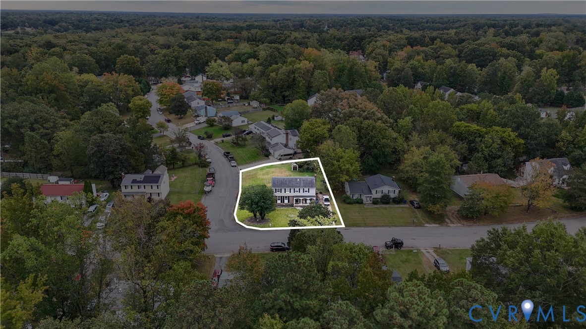 Aerial perspective of a detached residence featuring a corner lot, a multi-story exterior, an asphalt driveway, and mature landscaping