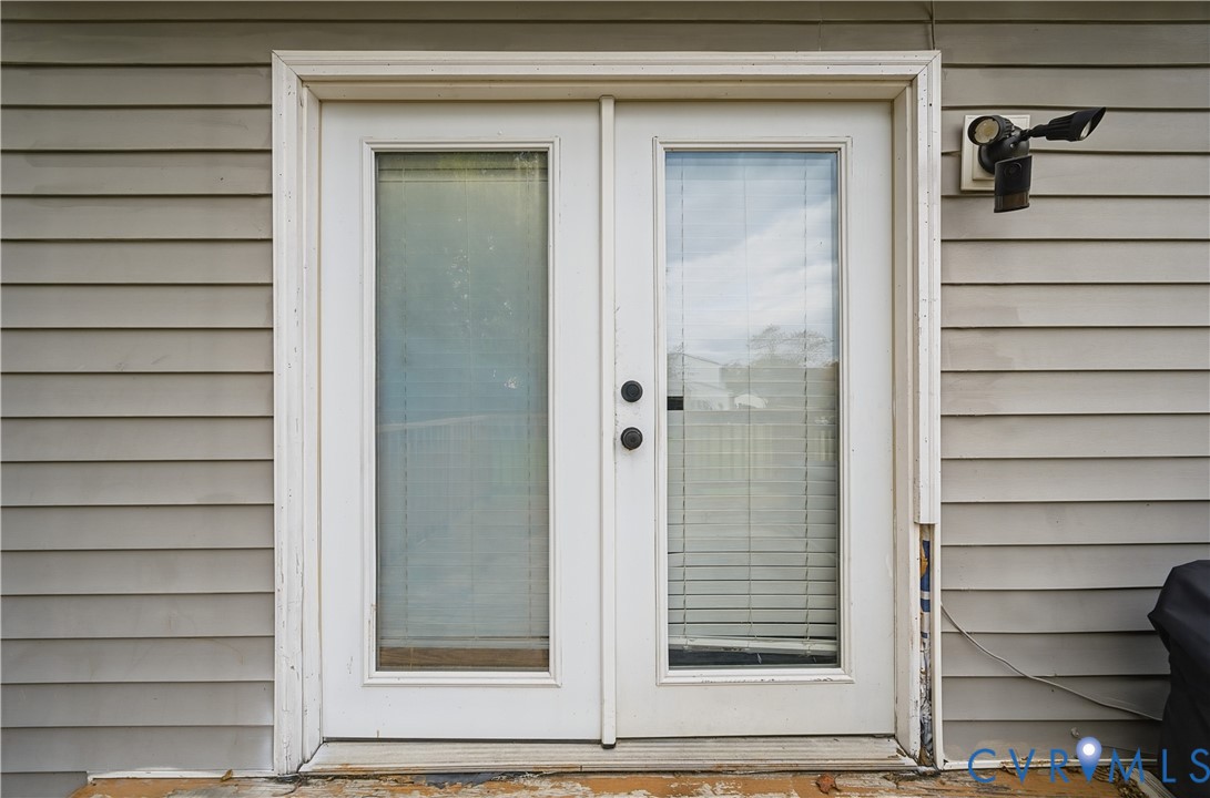 Double glass-panel doors featuring integrated blinds, horizontal lap siding, and exterior security lighting