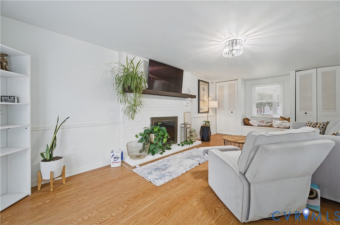 Living area featuring wood-finish flooring, a painted brick fireplace with a wood mantel, built-in shelving, a recessed window seat, and louvered-door cabinetry