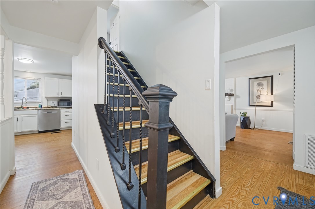 Staircase featuring wood-finish treads, a black-painted railing, and a decorative newel post, set against wood-finish flooring Staircase featuring wood-finish treads, a black-painted railing, and a decorative newel post, set against wood-finish flooring