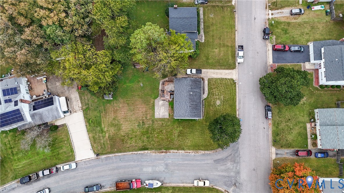 Aerial perspective of a property featuring a rectangular lot, mature canopy trees, an asphalt-paved driveway, and a rear patio area