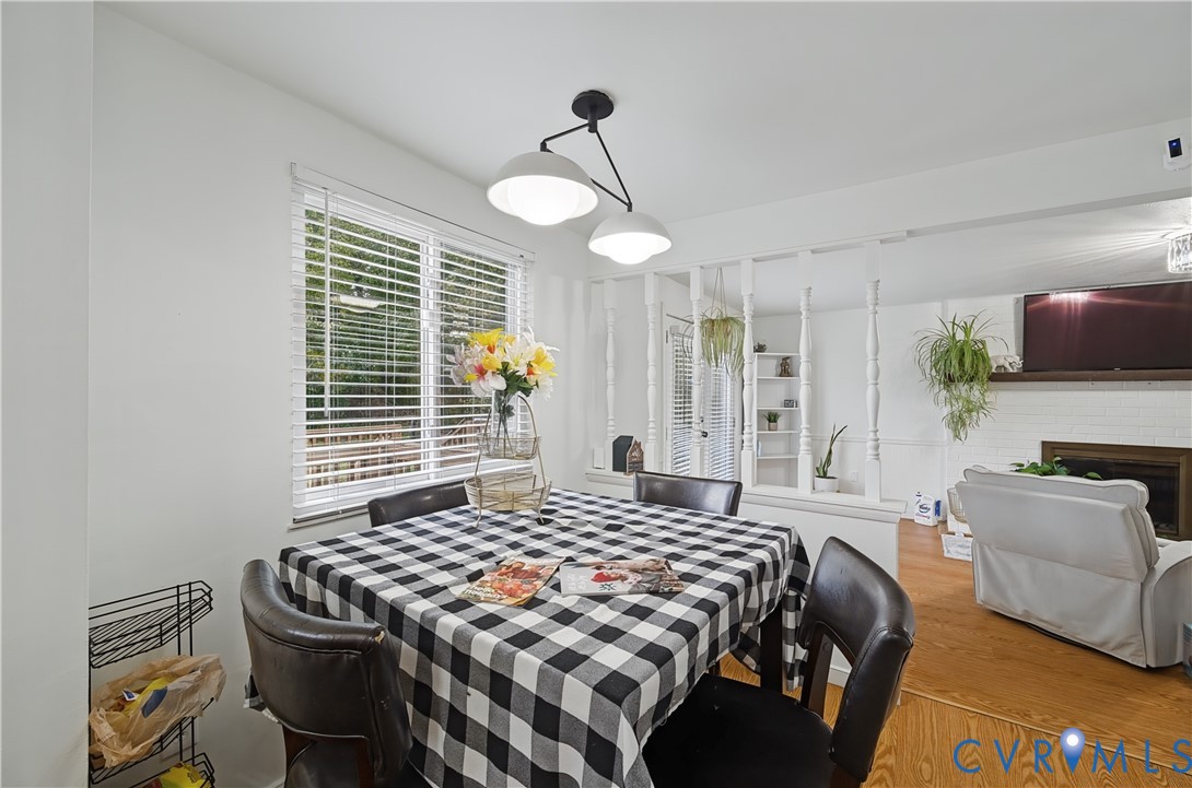 Dining area featuring a dual-globe pendant light fixture, horizontal slat window blinds, wood-finish flooring, and a decorative spindle room divider Dining area featuring a dual-globe pendant light fixture, horizontal slat window blinds, wood-finish flooring, and a decorative spindle room divider