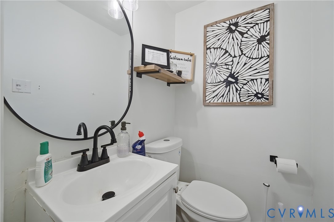 Round mirror with a black frame, white vanity with integrated basin, matte black faucet, and mounted wood-finish shelf