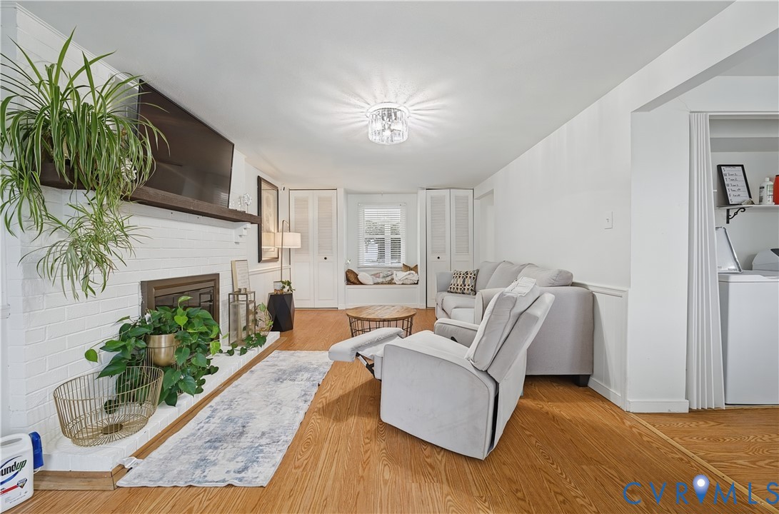 Painted brick fireplace with a wood mantel, wood-finish flooring, built-in window seat, ceiling-mounted light fixture, and louvered closet doors