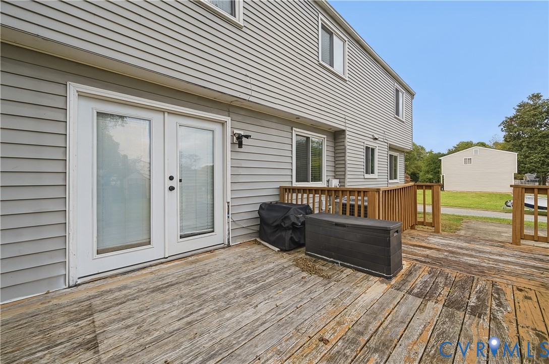 Exterior wood deck featuring a railing and double glass-paneled doors leading into the residence, complemented by horizontal vinyl siding