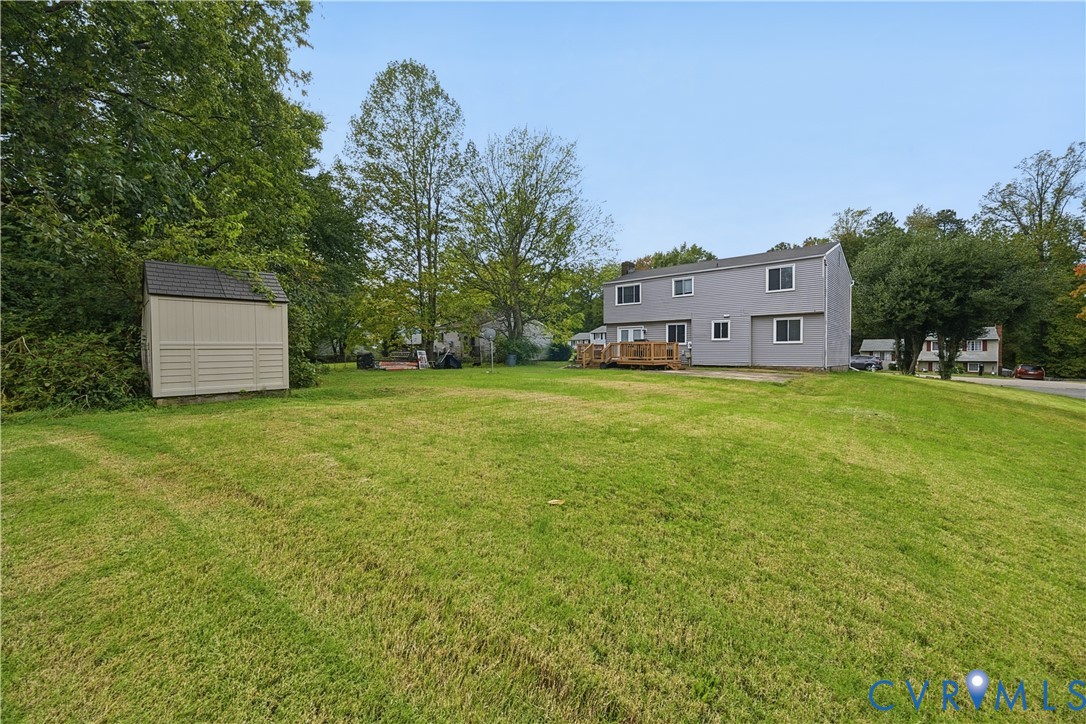 Expansive backyard featuring a large grass lawn, mature trees, a detached storage shed, and a wooden deck