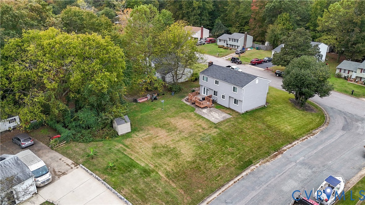 Two-story residence featuring light-toned siding, a rear wood deck, a concrete patio, a dedicated storage shed, and a spacious lawn area