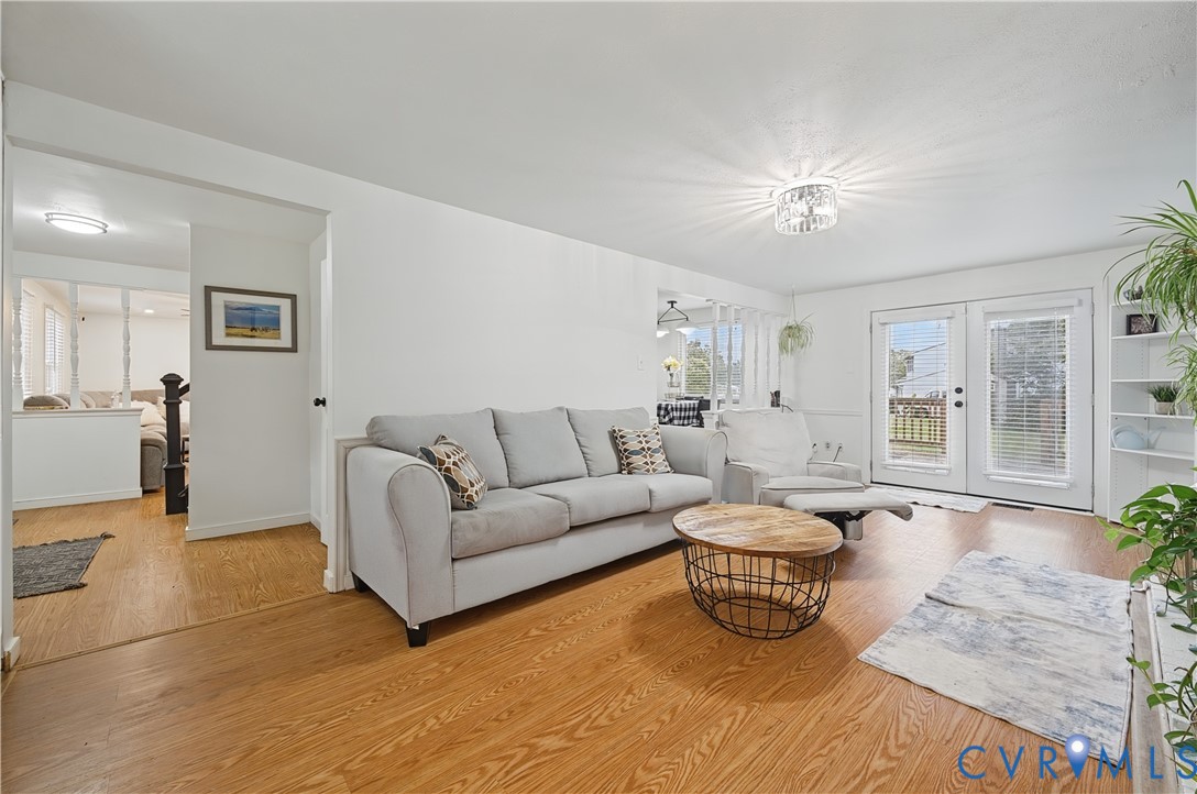 Living area featuring wood-finish flooring, white walls, built-in shelving, a glass-panel chandelier, and double doors providing exterior access