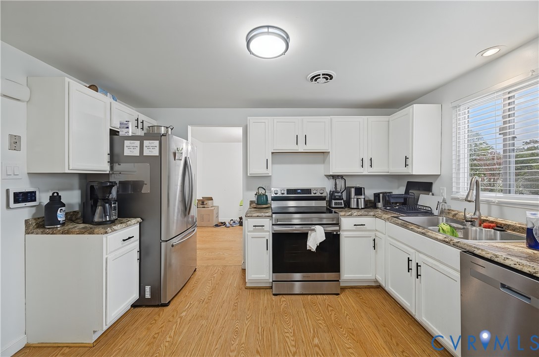 Kitchen featuring white shaker-style cabinetry, stainless steel appliances, speckled laminate countertops, and wood-finish flooring