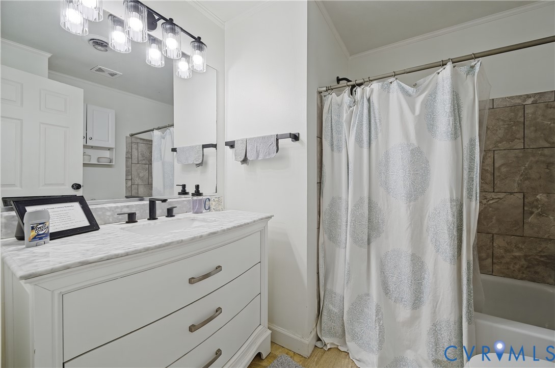 Bathroom vanity featuring a stone countertop, under-mount sink, matte black widespread faucet, multi-light vanity fixture, and large format tiled shower surround