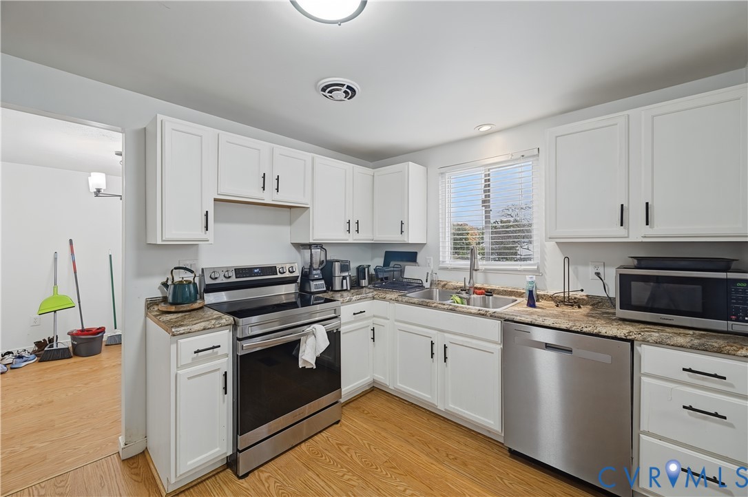 Kitchen featuring white Shaker-style cabinetry, stone-patterned countertops, wood-finish flooring, and stainless steel appliances