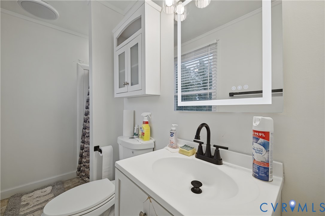 Bathroom vanity featuring a white cabinet, integrated sink, matte black faucet, and an illuminated wall-mounted mirror with an overhead light fixture and wall-mounted cabinetry