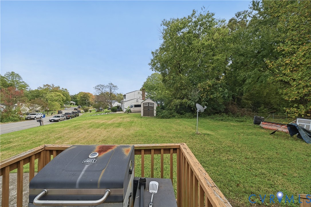 Outdoor wooden deck featuring a vertical slat railing, overlooking a sprawling grassy yard with mature trees and a detached storage shed