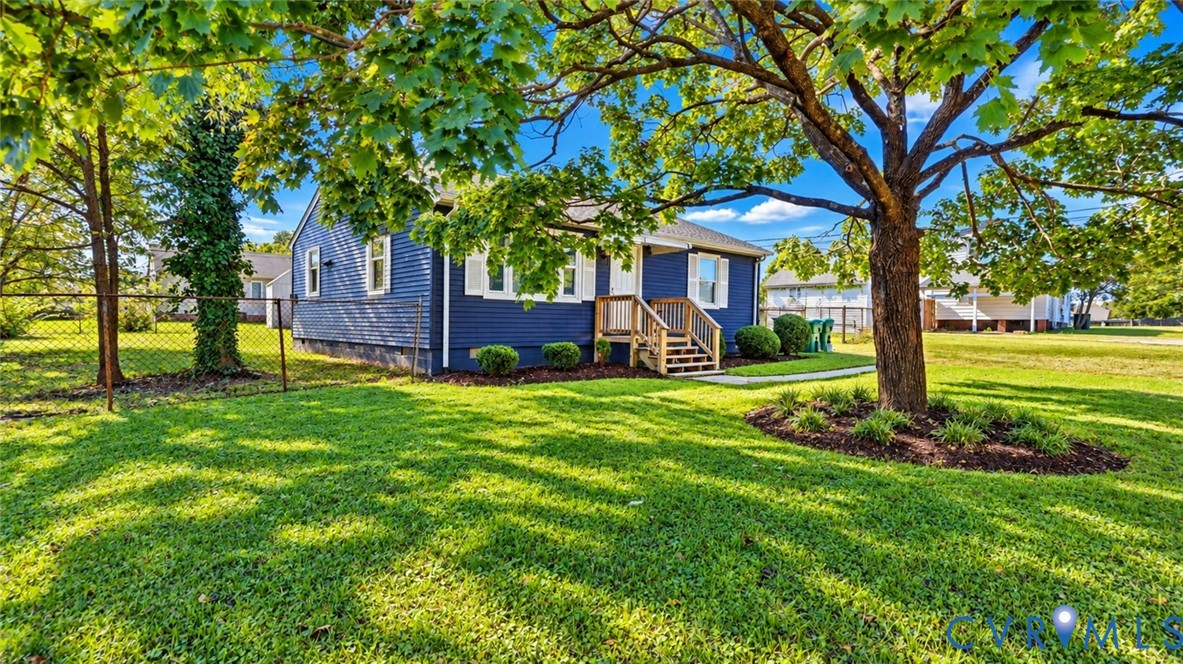 Blue-sided exterior featuring white shutters, a wood-constructed entry staircase, mature canopy trees, and an open lawn area Blue-sided exterior featuring white shutters, a wood-constructed entry staircase, mature canopy trees, and an open lawn area