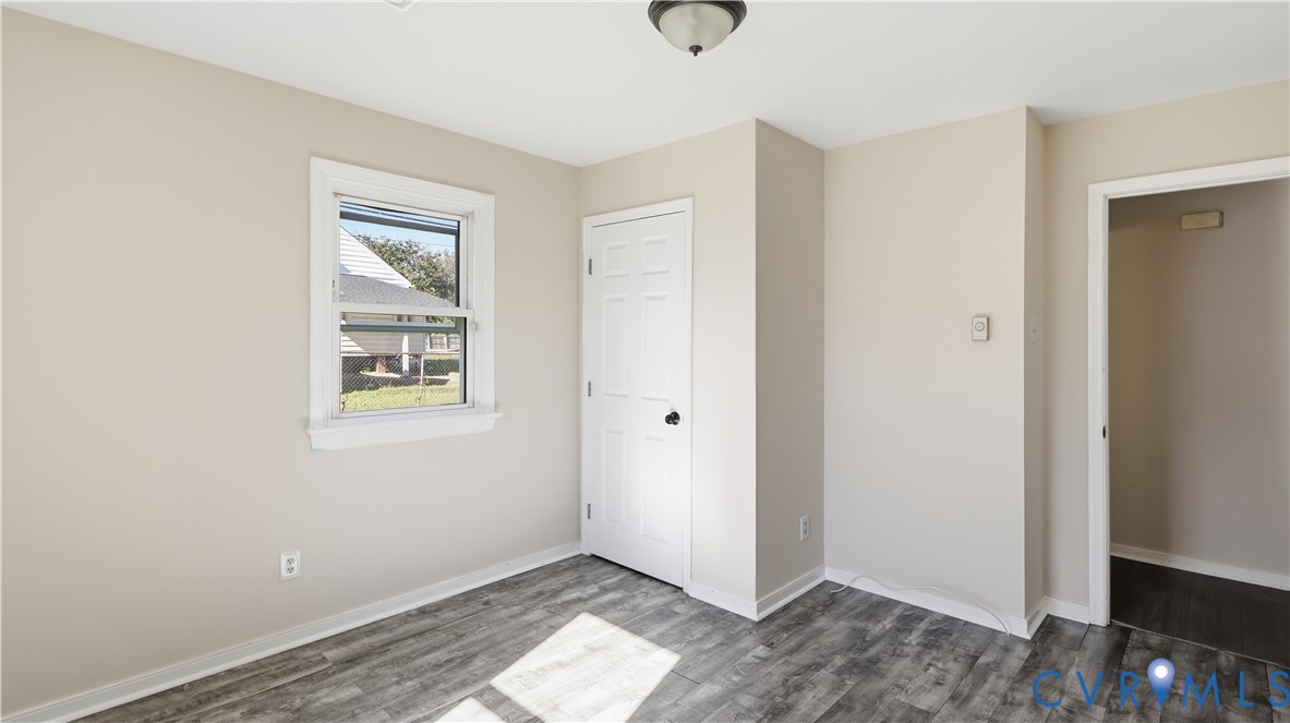 Neutral-toned interior room featuring wood-finish flooring, a single-hung window, a six-panel interior door, and a flush-mount ceiling light fixture