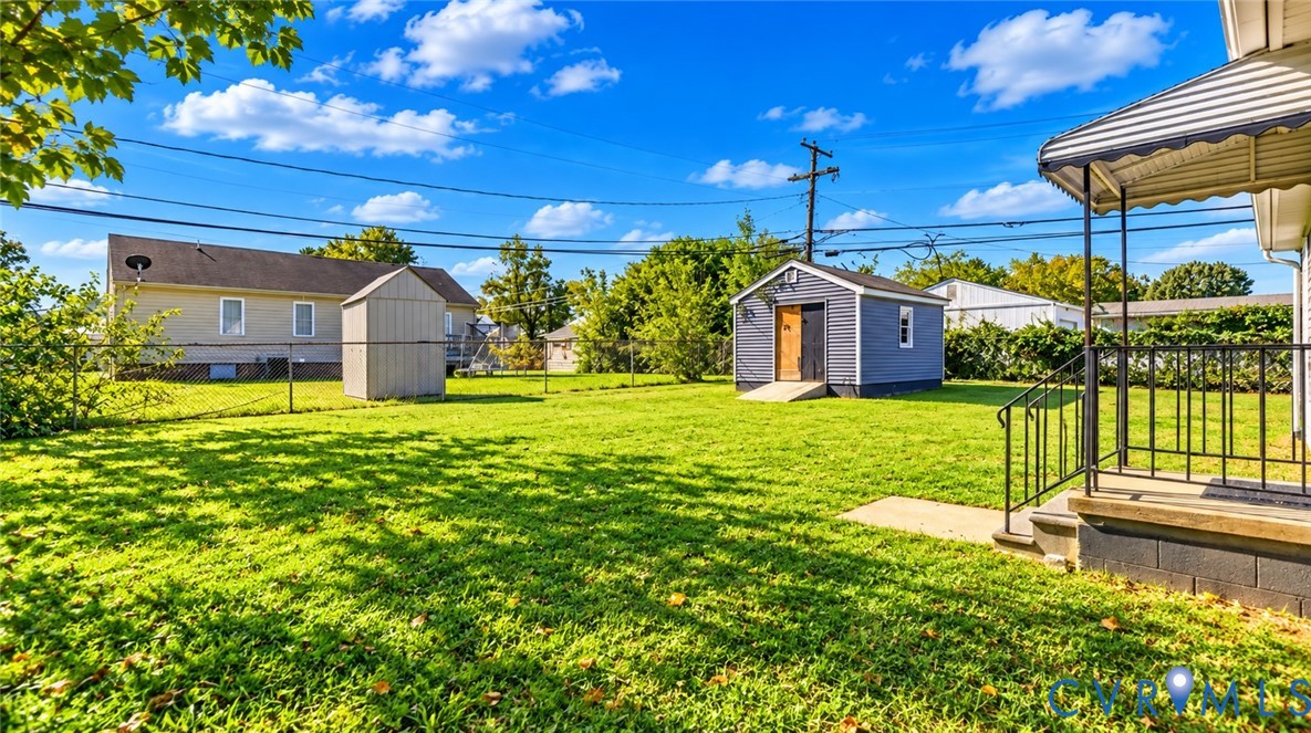 Expansive backyard featuring a level lawn, chain-link fencing, a detached storage structure, and a concrete-based porch with metal railings