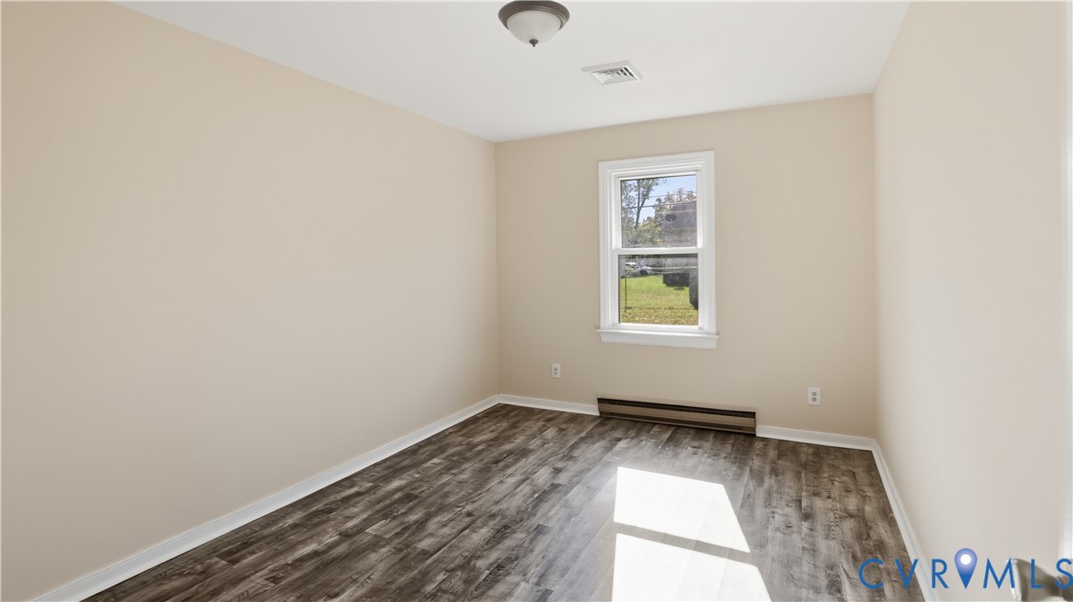 Neutral-toned interior space featuring wood-finish flooring, a single window, and a flush-mount ceiling light fixture
