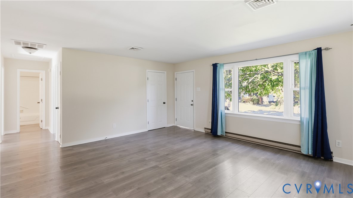 Neutral-toned interior space featuring wood-finish flooring, a multi-pane picture window, and white six-panel doors