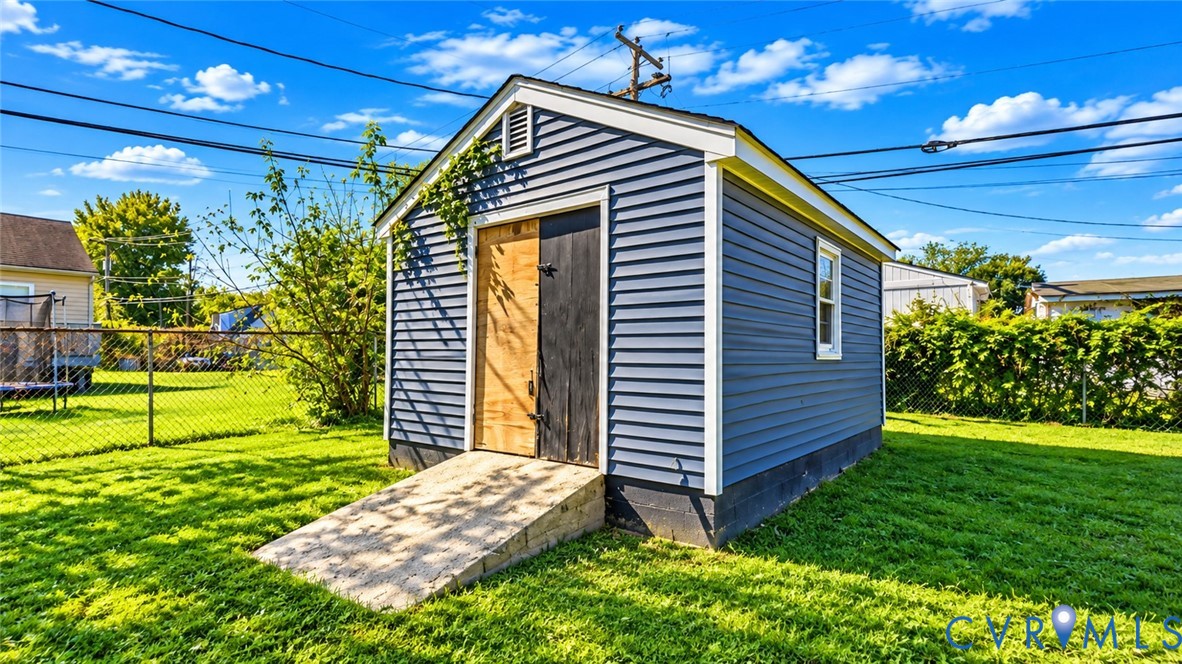 Detached exterior storage structure featuring blue siding, white trim, a gabled roofline, and an integrated wood-plank ramp